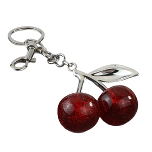 Sparkly red resin cherry keychain with silver metal leaves on a white background