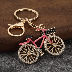 Pink rhinestone bicycle keychain with gold alloy finish and lobster clasp on wood background