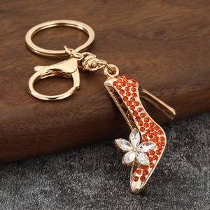 Detail shot of a golden high heel keychain with orange crystals and a white flower petal