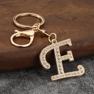 Close-up of gold letter E keychain with pavé rhinestones on walnut and stone background