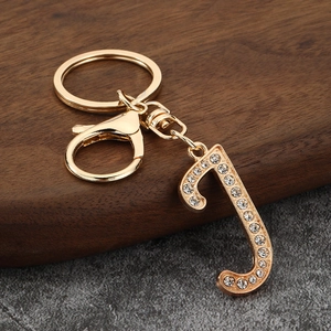 Detailed view of a gold-tone letter J keychain with clear rhinestones on a wooden stand
