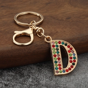 Golden D-letter keychain with colorful rhinestones on rustic wood and stone background