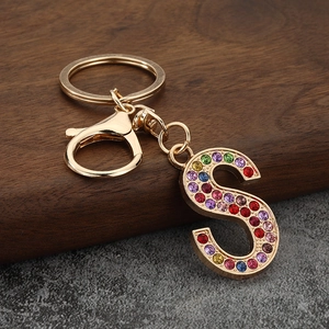 Detail of a golden S-shaped keychain with colorful rhinestones on a wooden base