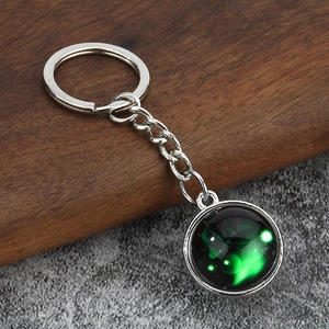 Close-up of a luminous zodiac keychain with green nebula glass pendant on wood surface