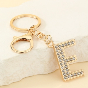 Detailed view of golden letter E keychain with sparkling crystals on stone background