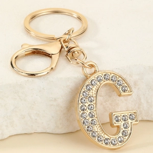 Detail of gold letter G keychain with sparkling white rhinestones on stone background