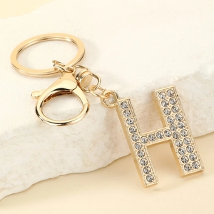 Close-up of golden letter H keychain with sparkling rhinestones on a marble base