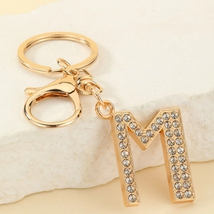 Macro detail of golden letter M keychain with crystal rhinestones on stone background