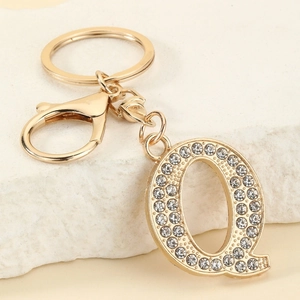 Close-up of gold-plated letter Q keychain with sparkling crystals on white marble