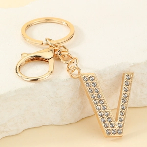 Close-up of golden letter V keychain featuring sparkling rhinestones on marble