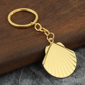 Minimalist golden shell pendant keychain with metallic texture on a neutral background