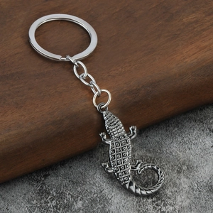 Realistic silver metal crocodile keychain with textured scales on wood and stone base