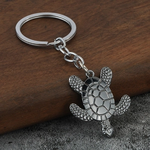 Silver turtle keychain with textured shell and flippers on a dark wood surface