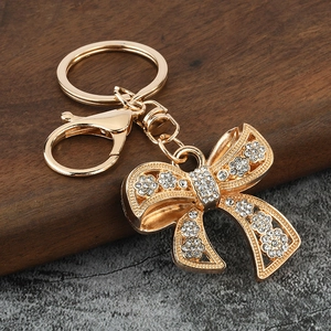 Golden bow pendant keychain with sparkling rhinestones and lobster clasp on stone surface