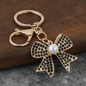 Detail of a gold-plated bow keychain with black rhinestones and a white imitation pearl