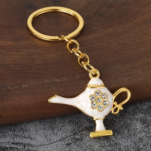 Detail of golden Aladdin lamp keychain with white enamel and rhinestone floral pattern