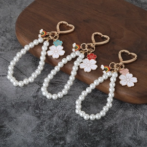 Three gold heart pearl keychains with white flower charms on a dark wooden tray