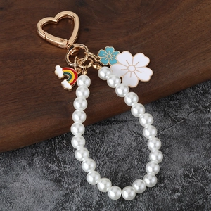 Beaded pearl keychain with white flower, rainbow cloud charms and heart clasp on stone surface