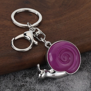 Detail of silver snail keychain with purple enamel shell on dark wood and stone