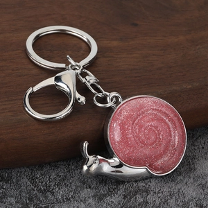 Pink glitter snail keychain with silver plating on rustic wood and stone background