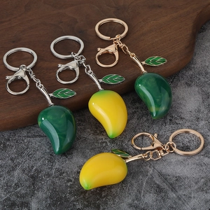Detail of colorful resin mango keychains with green enamel leaves on a wooden tray