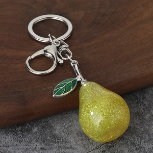 Macro detail of a glittery yellow resin pear keychain with a green leaf and silver lobster clasp