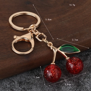 Minimalist red cherry keychain with gold chain and dimensions on rustic background