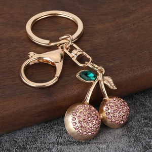 Golden cherry keychain with pink rhinestones and leaf detail on wooden background