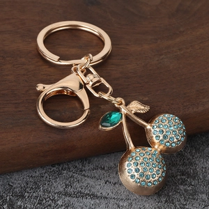 Detail of sparkling blue rhinestone cherry keychain with golden frame and emerald leaf