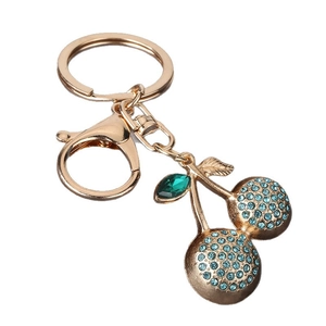 Golden cherry keychain with light blue rhinestones and green crystal leaf on white background