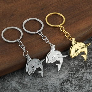 Polished shark-shaped metal keychains in gold and silver finishes on a stone background