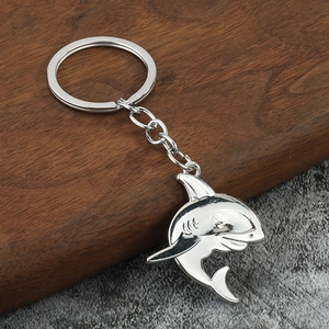 Polished silver metal shark pendant keychain with circular ring on a wooden surface