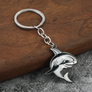 Macro detail of a 3D silver shark metal keychain on dark wood and stone texture