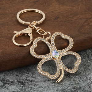 Golden four-leaf clover keychain with rhinestones and iridescent crystal on wood background