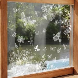 Detailed white floral and butterfly window clings on glass with soft garden background