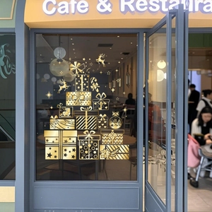 Close-up of golden Christmas window stickers with stacked gift boxes and reindeer on glass