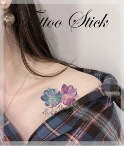Détail d'un tatouage éphémère floral avec fleurs bleues et violettes sur la clavicule