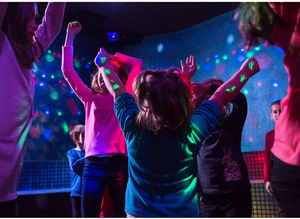Luminous temporary tattoos glowing green on kids dancing at a lively party scene