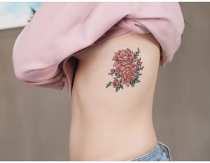 Détail de tatouage floral avec pivoine rose et feuilles vertes sur la taille d'une femme
