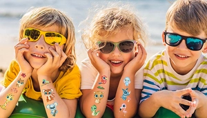Close-up of colorful cartoon animal glitter tattoos on children arms in beach setting