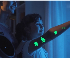 Luminous temporary tattoos showing glowing cartoon dinosaurs and stars on a child's arm
