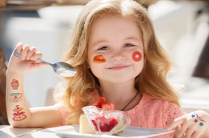 Close-up of waterproof cartoon cupcake and dessert tattoos applied on a child's face and arms