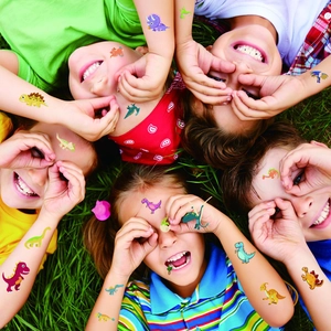 Five kids lying on grass showing colorful cartoon dinosaur temporary tattoos on arms