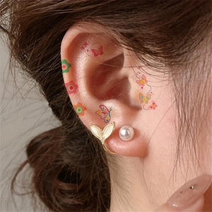 Close-up of gold mermaid tail ear cuff and pearl stud with colorful tattoo stickers