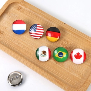 Detailed view of glossy national flag badges with metal back pins on a wooden tray