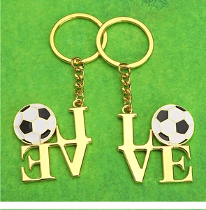 Close-up of gold LOVE football keychains set on a green turf field background