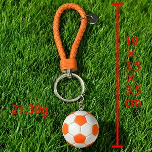 Detail of orange football keychain with leather cord on grass, weighing 21.39g