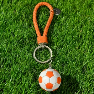 Detail of soccer ball keychain with orange braided leather strap on green grass background