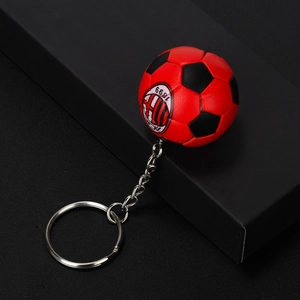 Detail of red and black soccer keychain with AC Milan logo on a dark background
