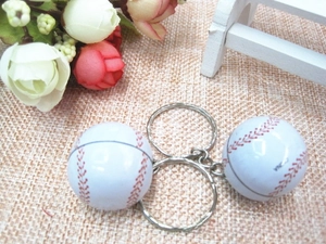 Close-up of white baseball keychains with red stitching on a woven texture background